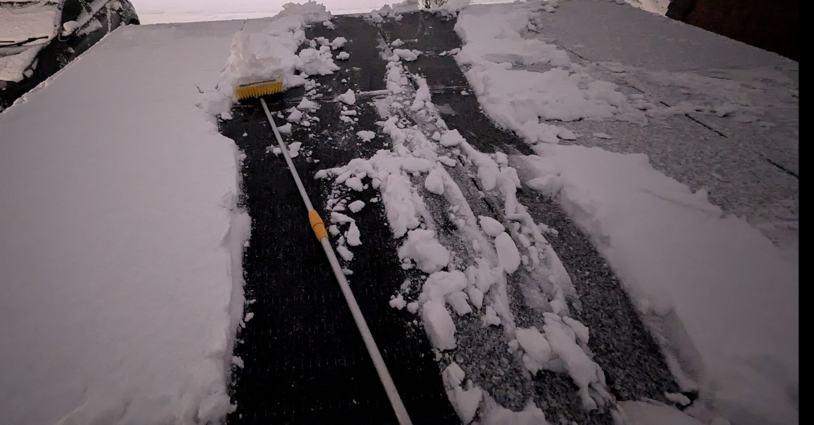 Clearing heavy wet snow from nearly flat solar panels on a gazebo roof with a long-handled broom