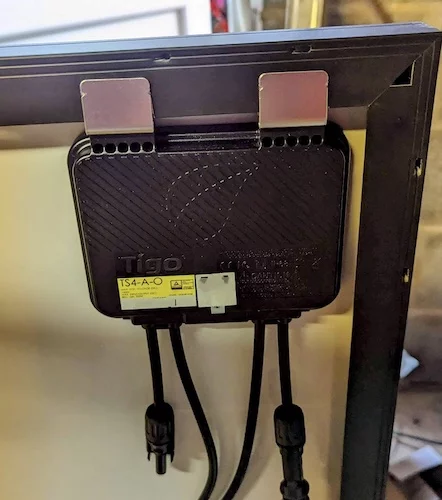 Photograph of a Tigo power optimiser clipped to that back of a solar panel. The panel is not yet installed.