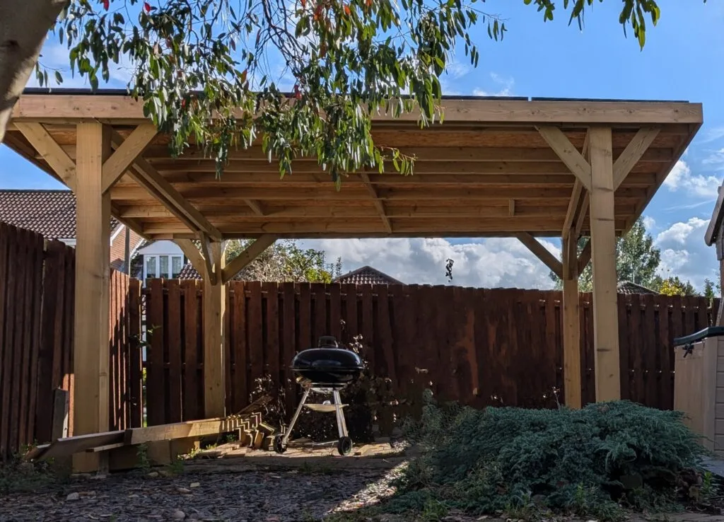 Completed timber gazebo with solar panels mounted on its roof, seen from underneath in a garden